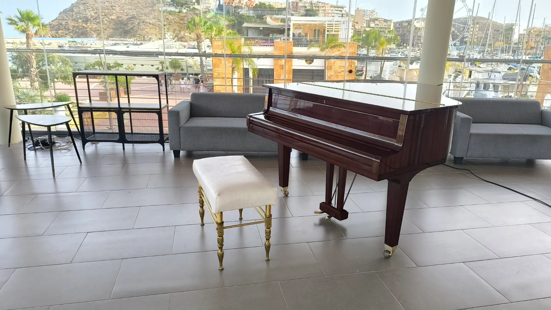 Sala de Mazmara Sunset con el piano frente a los ventanales y el puerto deportivo de Mazarrón al fondo